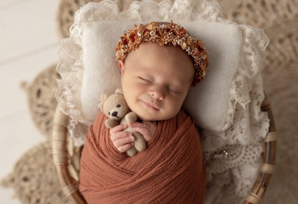 Schlafendes Neugeborenes mit Blumenkranz und kleinem Teddybären
